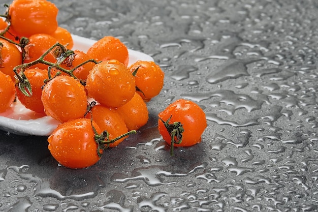 Tomate cereja laranja em gotas de água em uma mesa cinza closeup estilo escuro com espaço de cópia ingredientes para salada ou prato com foco seletivo de legumes