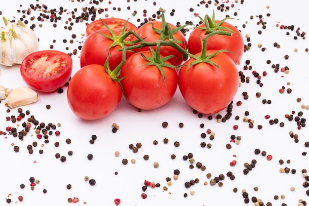 Tomates cercados por pimenta preta e vermelha e alho na superfície branca