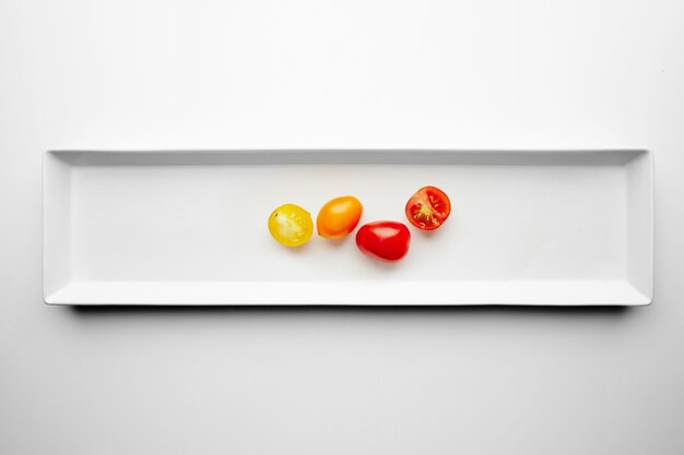 Tomates cereja amarelos e vermelhos isolados em um prato branco com metade dividida, vista superior
