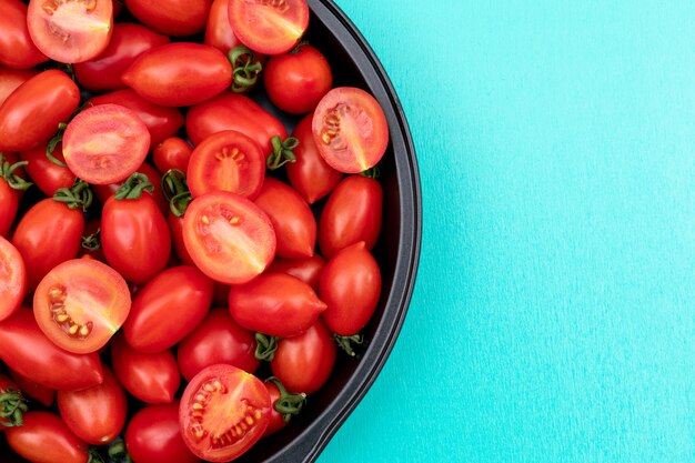 Tomates cereja frescos e saudáveis em uma tigela preta com espaço de cópia na superfície azul