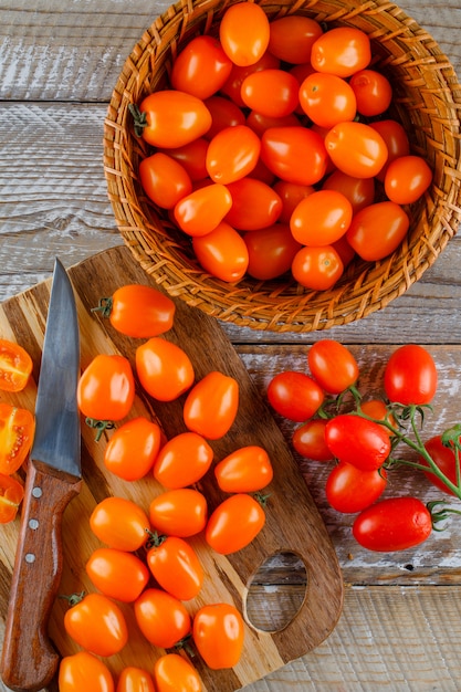 Tomates com faca em uma cesta na placa de madeira e de corte, vista superior.