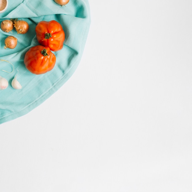 Tomates da herança com cebola e alho cravo no guardanapo azul contra um fundo branco