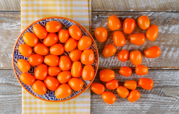 Tomates em um prato de madeira e toalha de cozinha. configuração plana.