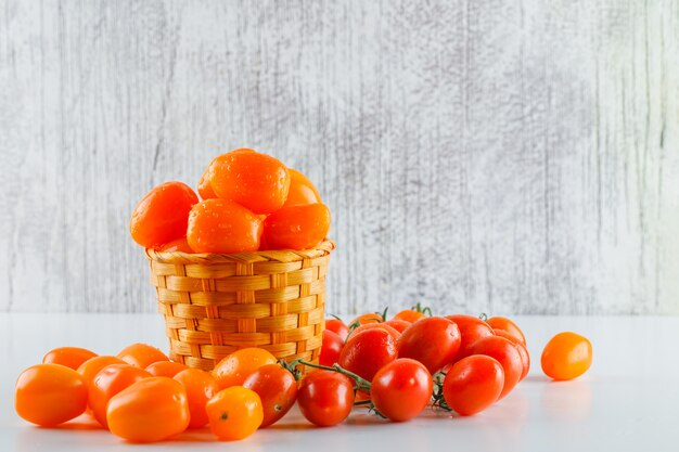 Tomates em uma cesta de vime na mesa branca e suja. vista lateral.