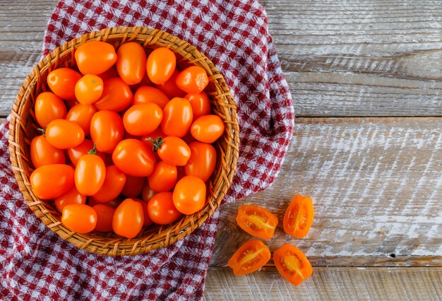 Tomates em uma cesta no pano de madeira e piquenique. configuração plana.