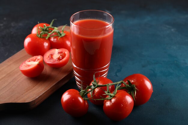 Tomates inteiros e cortados e um copo de suco de tomate.