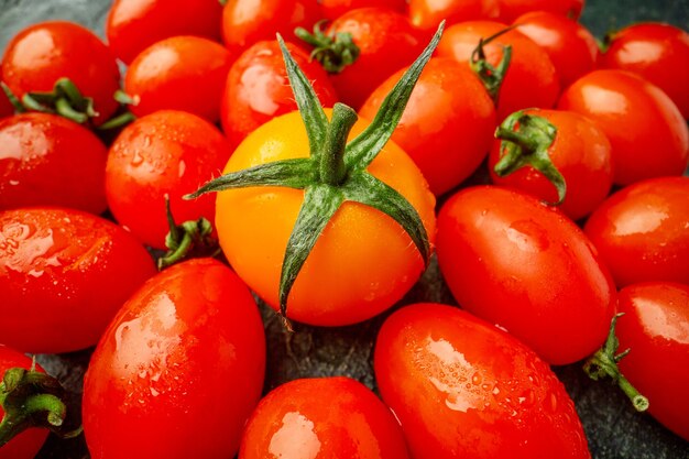 Tomates laranja de frente com tomates vermelhos em uma superfície verde escura