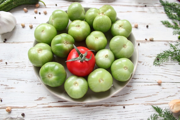 Tomates verdes, picles na mesa de madeira branca com verde e vermelho e pimenta, erva-doce, sal, pimenta preta, alho, ervilha, close-up, conceito saudável, vista superior, configuração plana