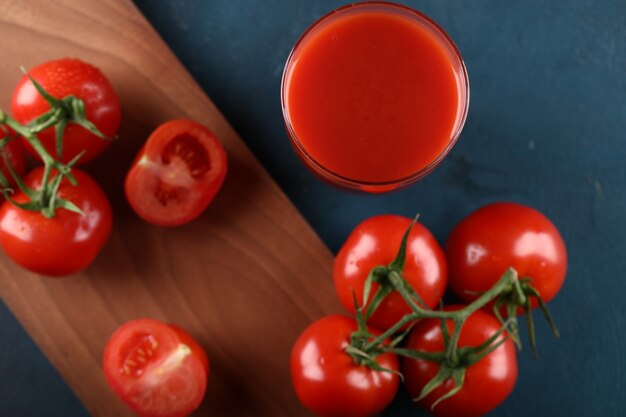 Tomates vermelhos e um copo de suco em uma placa de madeira. Vista do topo.