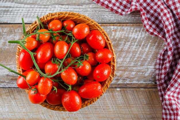 Tomates vermelhos em uma cesta de vime em madeira e toalha de cozinha. configuração plana.