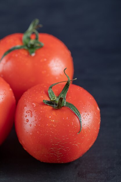 Tomates vermelhos frescos em uma superfície escura.