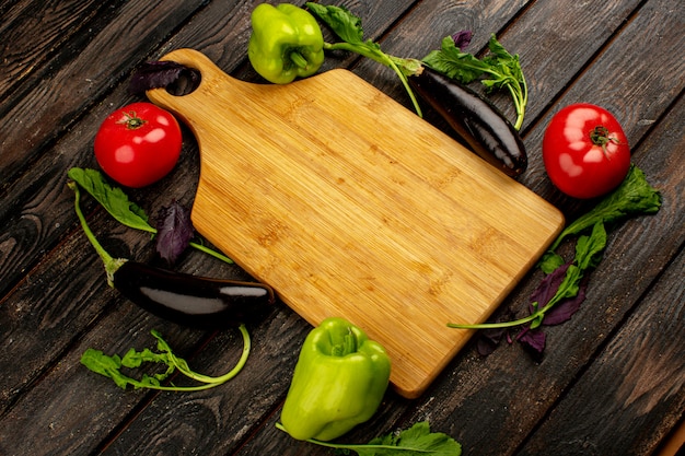 Tomates vermelhos frescos maduros com pimentão verde e berinjela preta, juntamente com verduras e mesa marrom sobre um piso de madeira