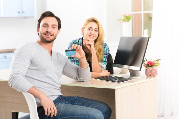 Tons de jovem feliz e alegre, mostrando o cartão de crédito para a câmera. Homem e mulher sorrindo para a câmera enquanto trabalhava no interior do escritório.