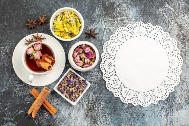 Top shot de chá de ervas com três tigelas de flor seca e um pedaço de renda em cinza