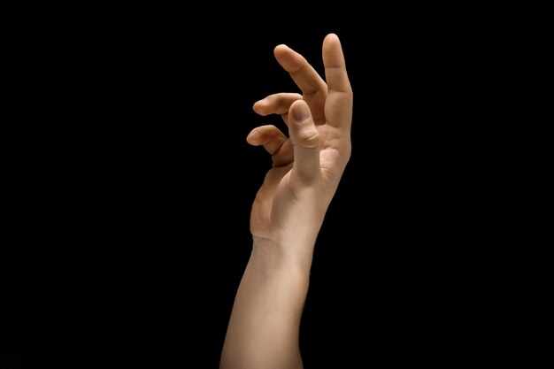 Toque de luz. Mão masculina, demonstrando um gesto de contato isolado no fundo preto do estúdio. Conceito de emoções humanas, sentimentos, ficologia ou negócios.