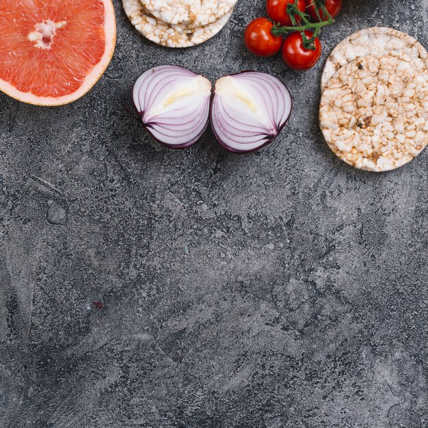 Toranja cortada ao meio; cebola; bolo de arroz tufado e tomate cereja em um velho cenário cinza