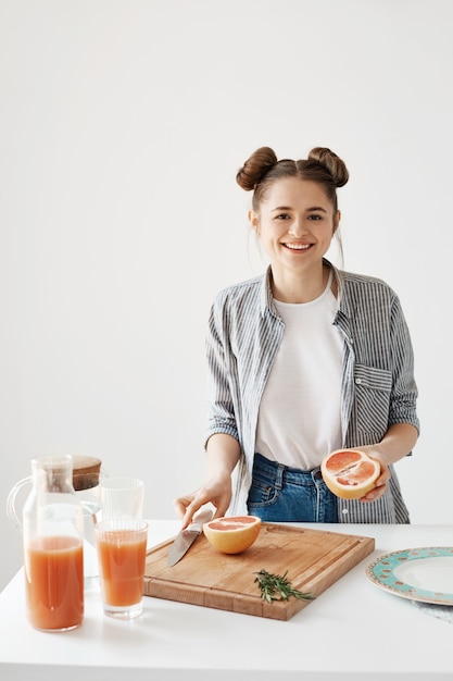 Toranja de sorriso do corte da menina bonita alegre para o café da manhã sobre a parede branca. Smoothie de desintoxicação saudável. Comida de fitness.