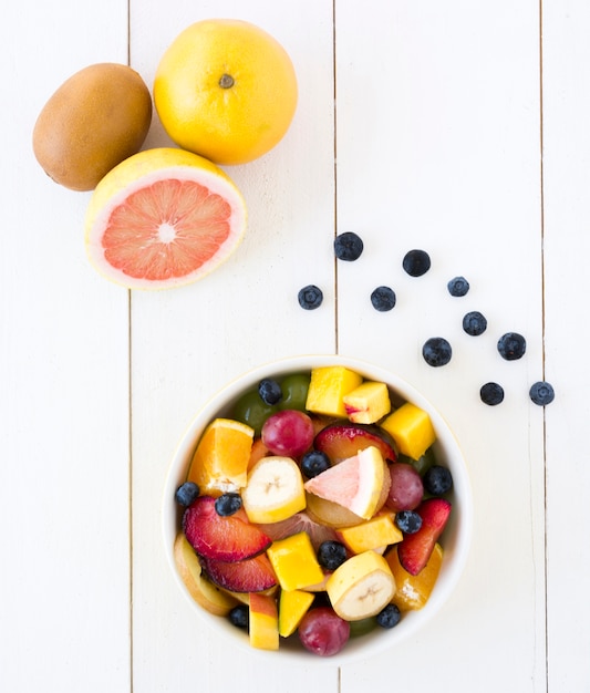 Toranja; kiwi e mirtilos com tigela de salada de frutas na mesa de madeira branca