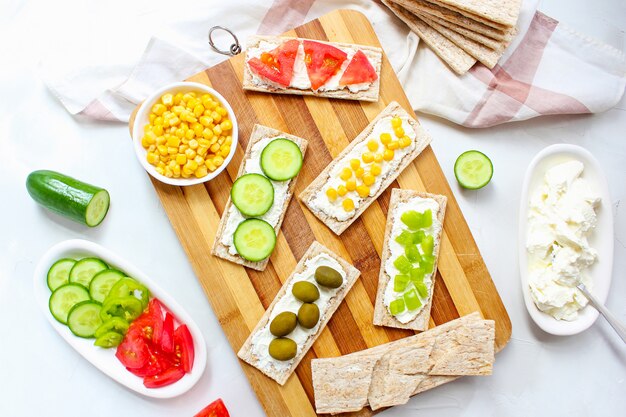 Torrada caseira com queijo cottage e azeitonas verdes, fatias de repolho, tomate, milho, pimenta verde na tábua. Conceito de comida saudável, vista superior. Configuração plana