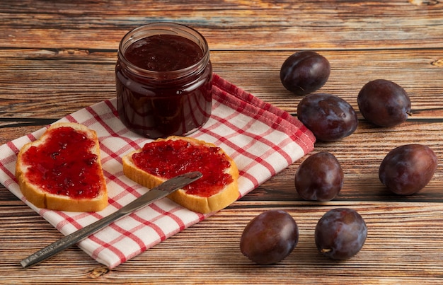 Torradas com confiture de ameixa em frasco de vidro sobre toalha xadrez.