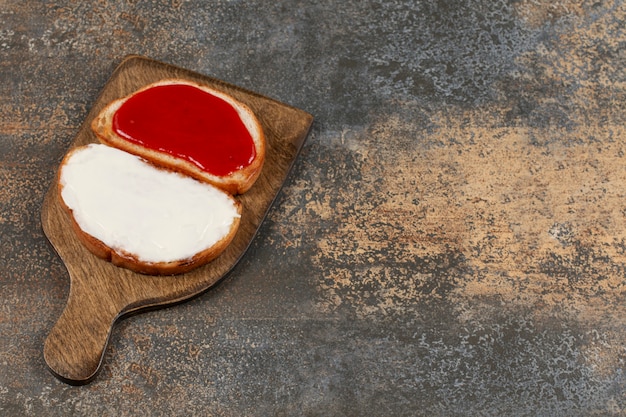 Torradas com geléia e creme de leite na tábua de madeira.