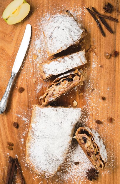 Torta de maçã austríaca tradicional - Apfelstrudel com maçãs, nozes, canela e passas, strudel fatiado em uma tábua de madeira, vista superior.