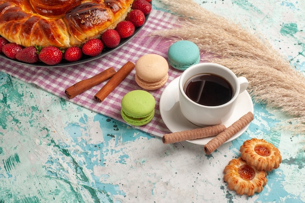 Torta doce gostosa de vista frontal com macarons franceses de morangos vermelhos e chá na superfície azul