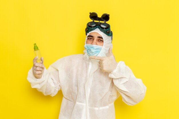 Trabalhador científico masculino de vista frontal em traje de proteção especial segurando um frasco de spray na superfície amarela