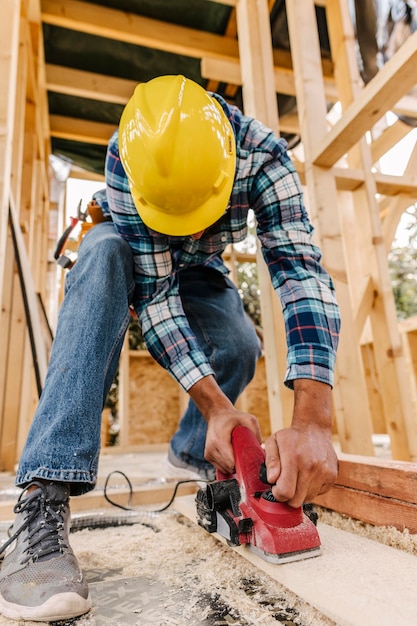 Foto grátis trabalhador da construção civil com capacete lixando pedaço de madeira