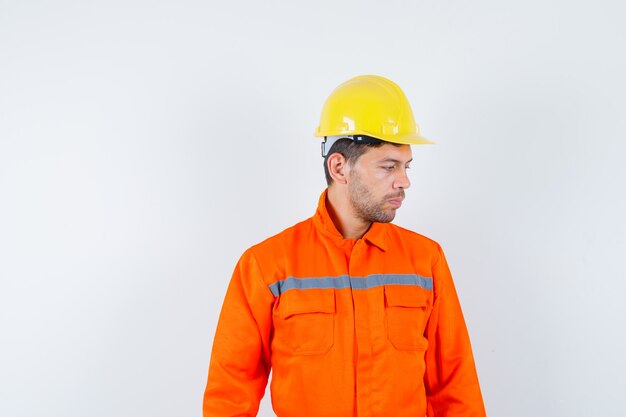 Trabalhador da construção civil de uniforme, capacete olhando para baixo e olhando pensativo, vista frontal.