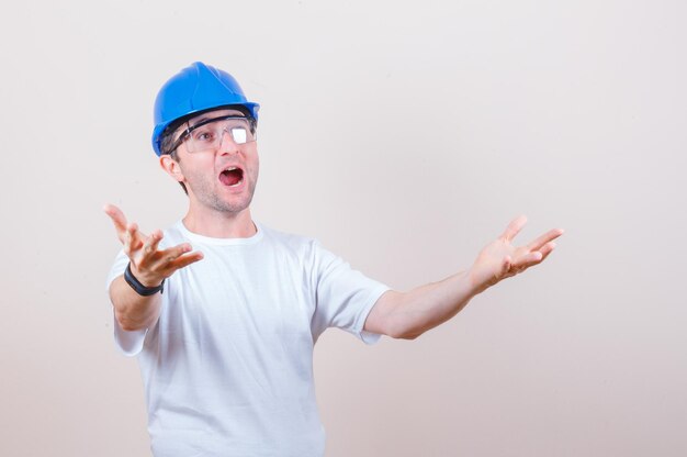 Trabalhador da construção civil esticando as mãos em uma camiseta, capacete e parecendo surpreso