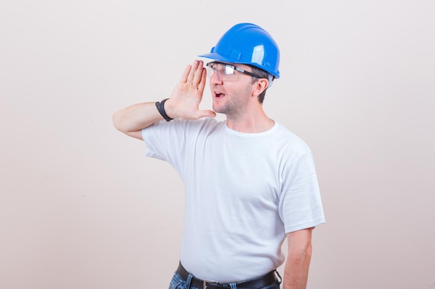Trabalhador da construção civil gritando para alguém de camiseta, jeans, capacete