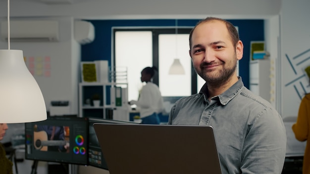 Trabalhador de editor de vídeo em frente à câmera, sorrindo, trabalhando no escritório da agência criativa, segurando la ...