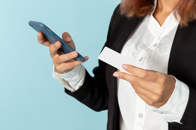 Trabalhador de escritório feminino com vista frontal usando o telefone e segurando o cartão na superfície azul