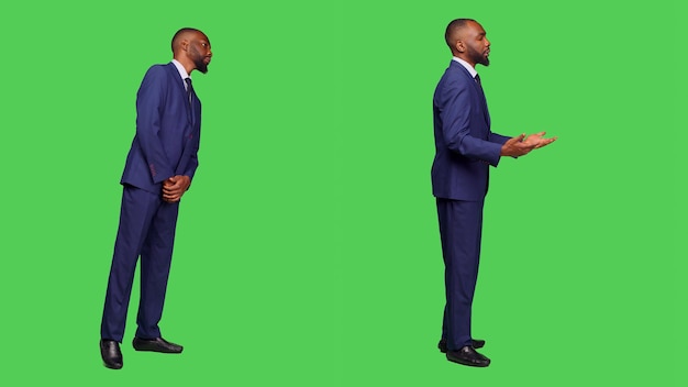 Foto grátis trabalhador de escritório masculino em terno formal esperando no estúdio, olhando ao redor sobre tela verde de corpo inteiro. empregado de startup se sentindo confiante e elegante na câmera, fundo de tela verde.