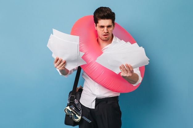 Foto grátis trabalhador de escritório olha um monte de documentos com descontentamento. cara sai de férias e posa com círculo inflável e máscara de natação.