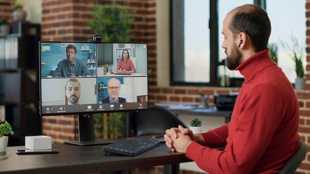 Foto grátis trabalhador de escritório participando de reunião de videochamada com empresários, falando sobre crescimento financeiro. funcionário do sexo masculino usando bate-papo por videoconferência remota para discutir sobre comunicação sem fio. tiro de tripé.