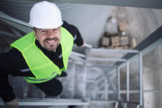 Trabalhador de fábrica industrial em equipamento de proteção em pé na escada de metal da fábrica