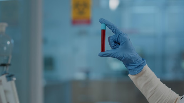 Trabalhador de laboratório segurando substância vermelha em tubo de ensaio para análise científica, trabalhando com dna em laboratório. engenheiro químico com luvas usando frasco de vidro para analisar líquido em vidraria. fechar-se Foto Premium
