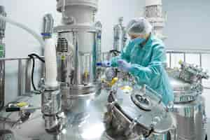 Foto grátis trabalhador de mulher fábrica farmacêutica em roupas de proteção operando a linha de produção em ambiente estéril
