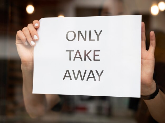 Trabalhador de restaurante colocando uma placa de comida para viagem na frente do restaurante