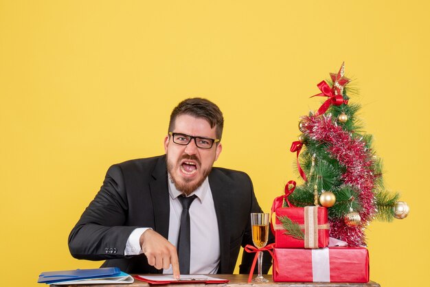 Trabalhador do sexo masculino de vista frontal atrás de sua mesa com presentes e a árvore de natal gritando em amarelo