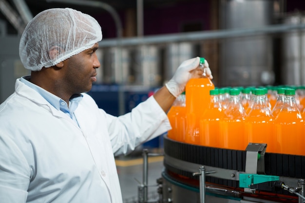 Foto grátis trabalhador do sexo masculino verificando garrafas de suco na fábrica