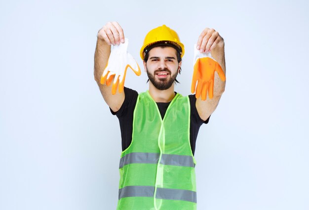 Trabalhador em capacete amarelo tirando e demonstrando suas luvas de oficina.