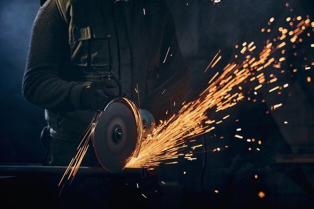 Trabalhador em luvas de proteção polindo metal com faíscas