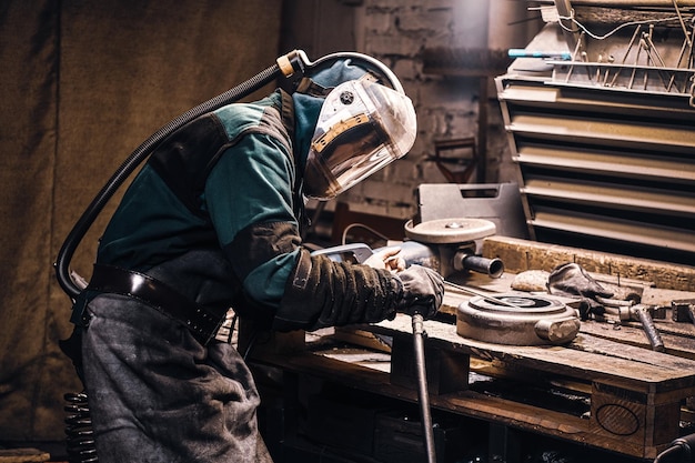 Trabalhador experiente está consertando peças de metal para máquina-ferramenta na fábrica ocupada.