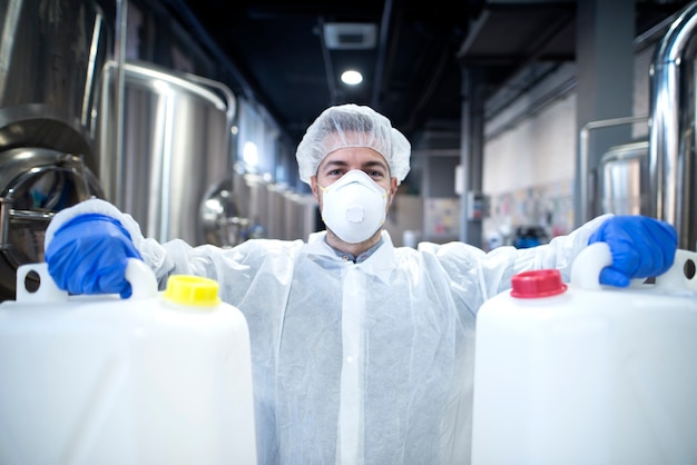 Foto grátis trabalhador industrial com máscara protetora e uniforme branco segurando latas de plástico para indústria química