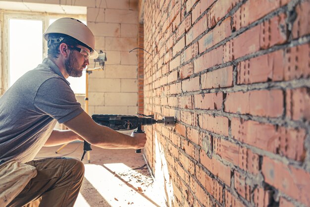 Trabalhador manual em um canteiro de obras no processo de perfuração de uma parede com um perfurador