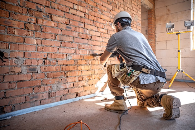 Trabalhador manual em um canteiro de obras no processo de perfuração de uma parede com um perfurador