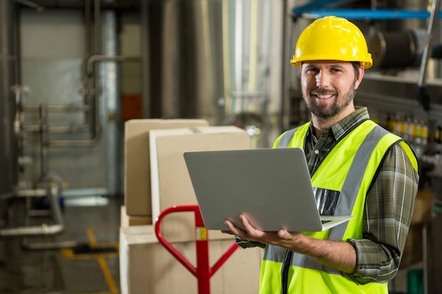 trabalhador masculino sorridente usando laptop em armazém de distribuição